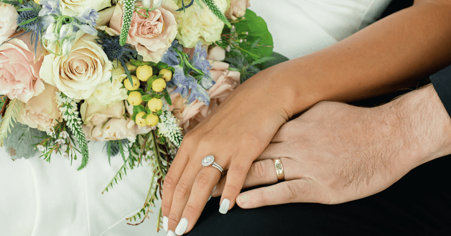 Bride_and_groom_on_wedding_day_showing_hands_with_rings_and_bridal_bouquet
