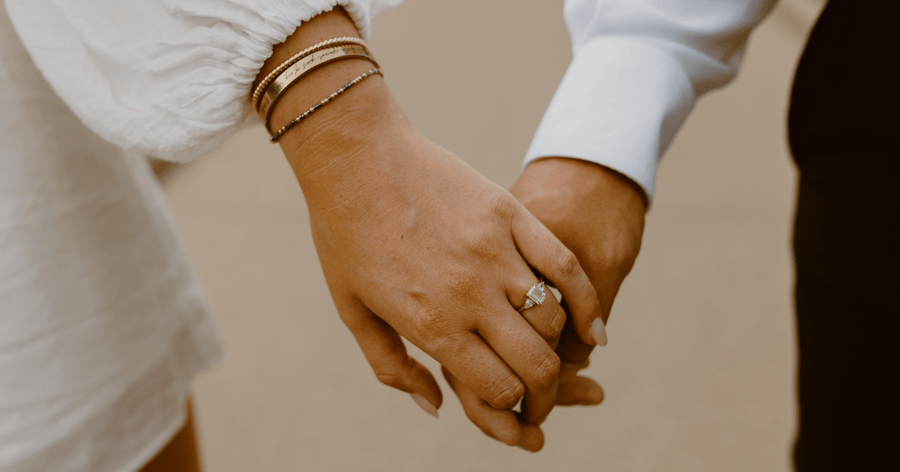 Couple_holding_hands_showing_bracelets_and_emerald_engagement_ring_accented_with_pear_side_stones