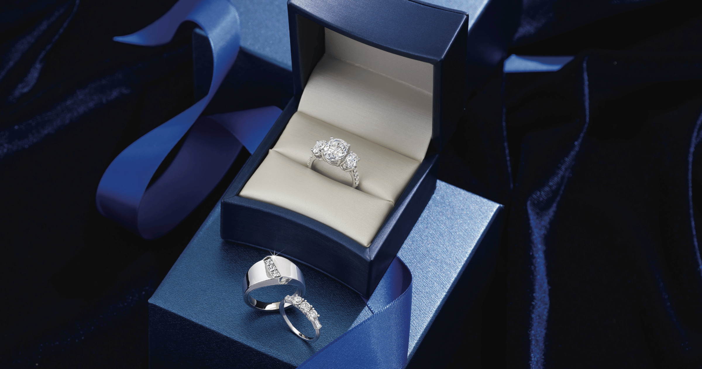 White_Gold_(or_Platinum)_Accented_Engagement_Ring_and_Matching_Wedding_Band_shown_with_Complementing_Mens_Wedding_Band_in_navy_blue_ring_box_with_ribbon