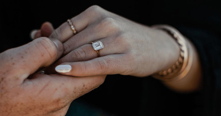 Yellow Gold Bezel Set Engagement Ring set with an Emerald Cut Diamond shown on Left Hand Ring Finger