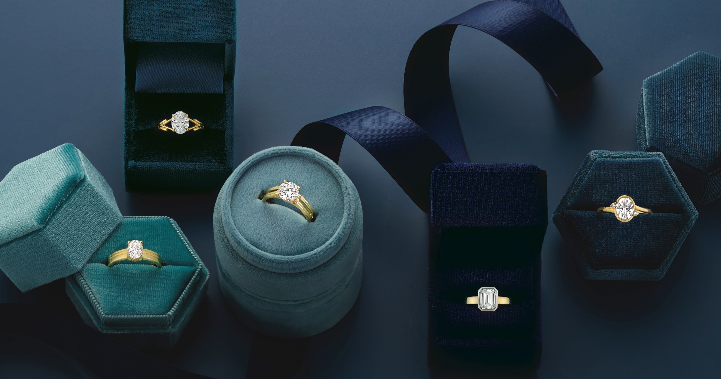 Various Yellow and White Gold Engagement Rings in Blue Ring Boxes with Navy Background with Navy Ribbon