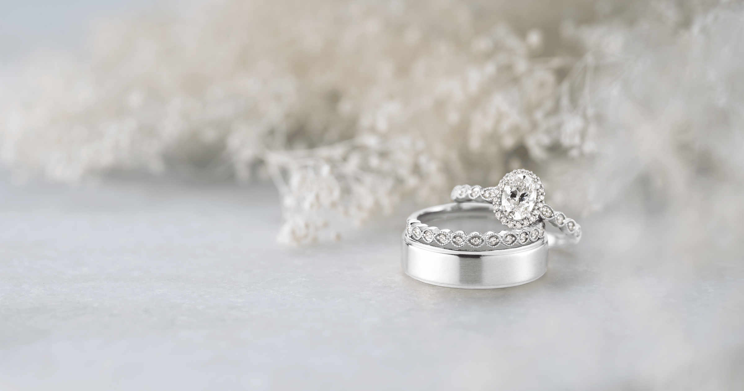 White Gold (or Platinum) Diamond Halo Engagement Ring with Pavé Accent Stones set with an Oval Cut Diamond; Matching White Gold (or Platinum) Accented Wedding Band; Men's White Gold (or Platinum) Beveled Edge Wedding Band